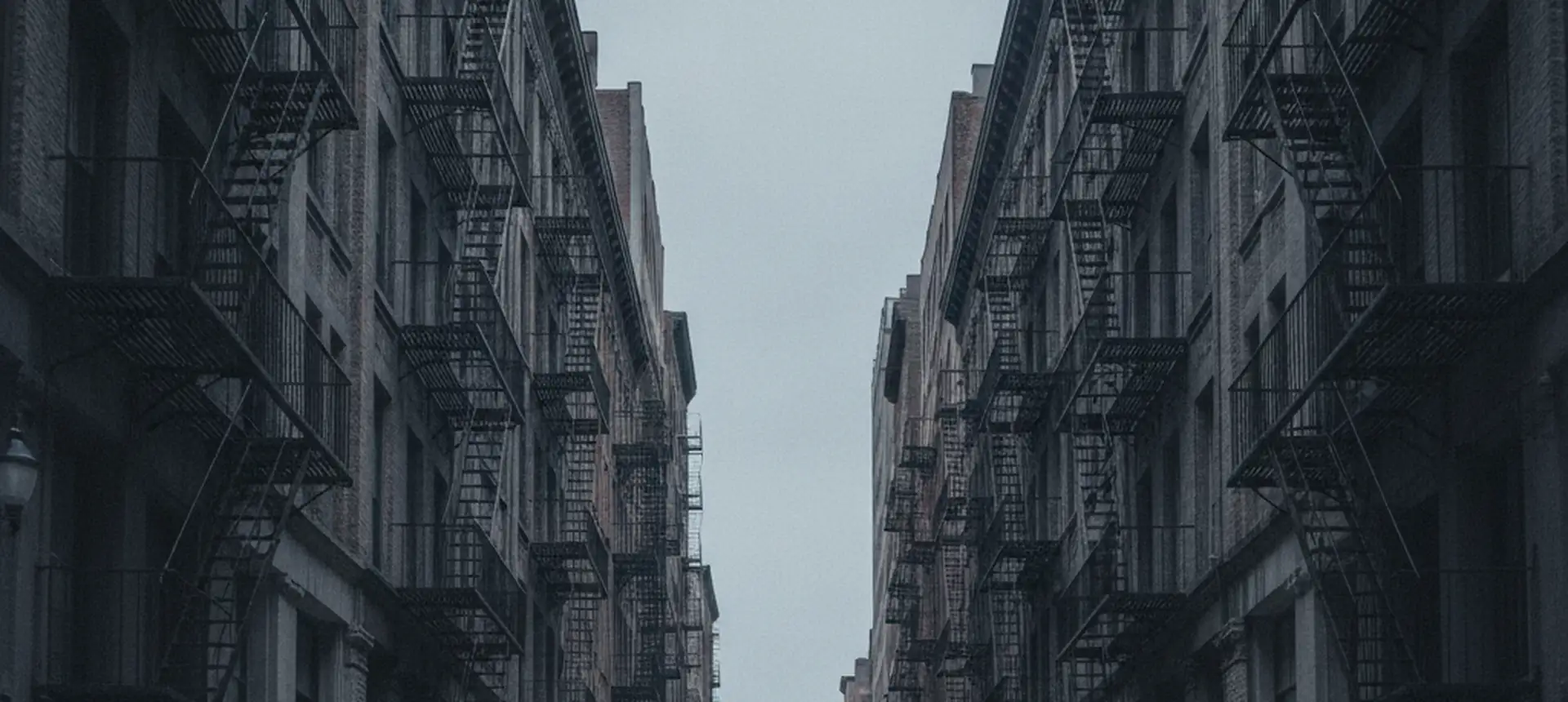 A narrow downtown street of cast-iron loft buildings with fire escapes in deep perspective.